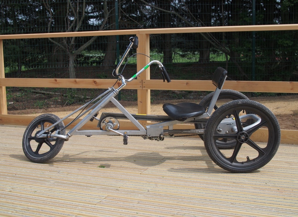 A silver adult size recumbent cycle on a wooden platform