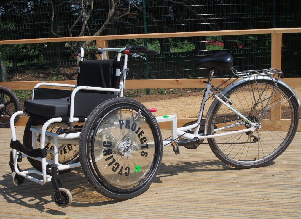 A white adult size wheelchair cycle on a wooden platform